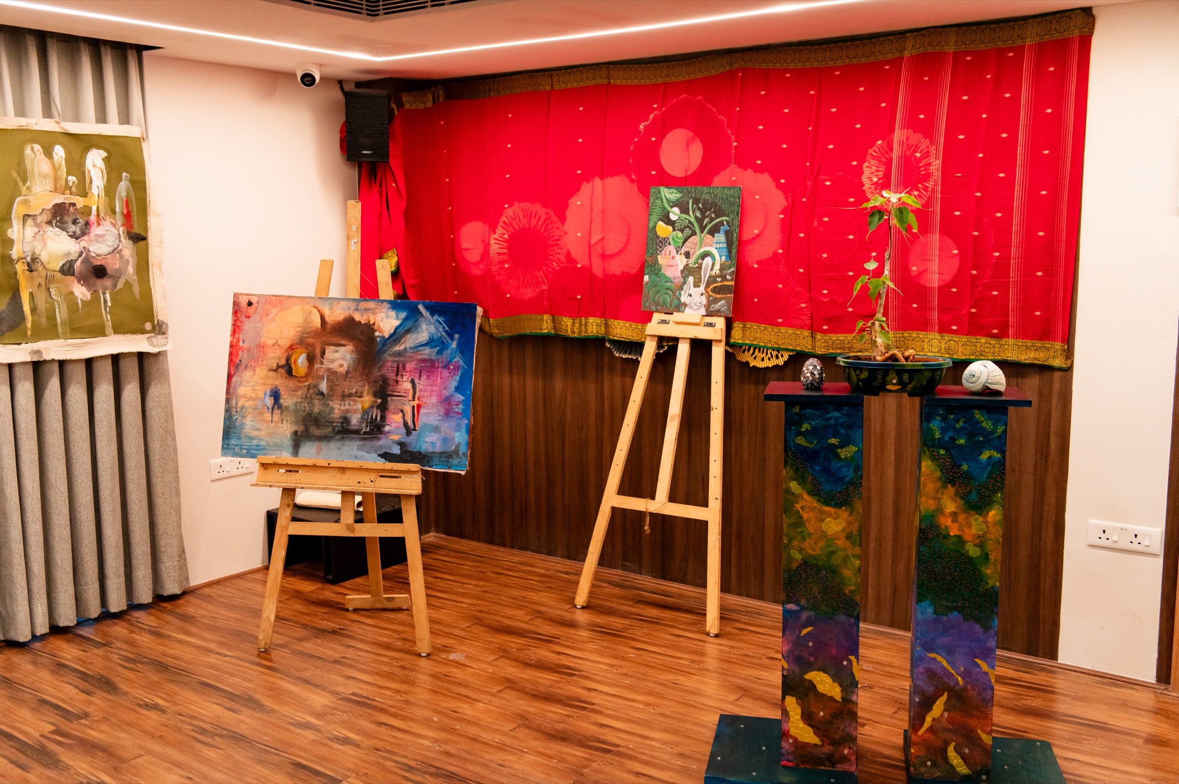 Paintings and sculptural works installed against a red textile backdrop in The Gallery.